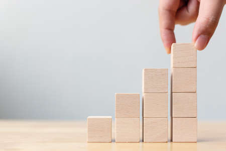 Hand arranging wood block stacking as step stair. Ladder career path concept for business growth...