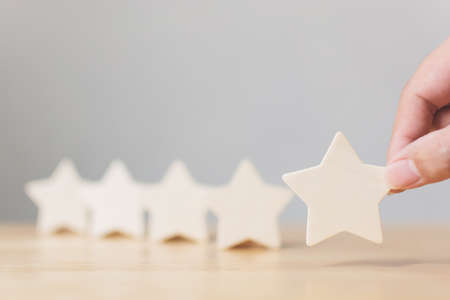 Hand putting wooden five star shape on wood table. The best excellent business services rating customer experience conceptの写真素材