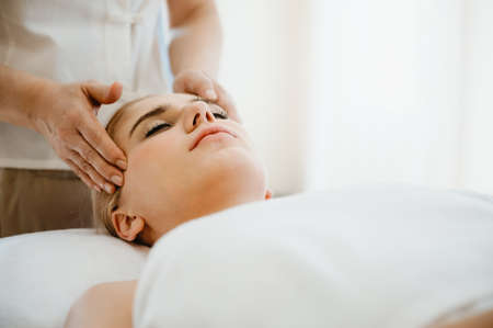 Beautiful woman receiving head and facial massage in spa salon. Concept of body health care and traditional thai massage relaxの写真素材
