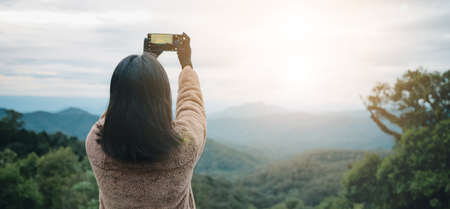Asian woman take a photo by smartphone on mountain in thailand. She wear sweater and gloveの写真素材