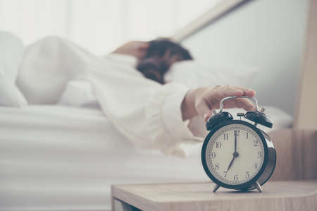 Young asian woman wake up early in morning. She lying on bed and trying turn off alarm clockの写真素材