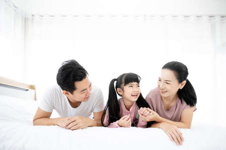 Happy asian family people leisure in bedroom together. Father and mother with daughter relaxing on bed and enjoy funnyの写真素材