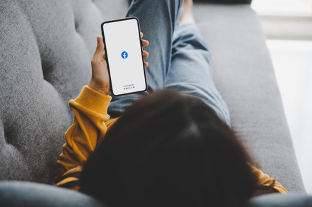 BANGKOK, THAILAND - September 9, 2020 : Asian woman using mobile with facebook application on the screen on sofa at home. Social media are using for information sharing and networkingのeditorial素材