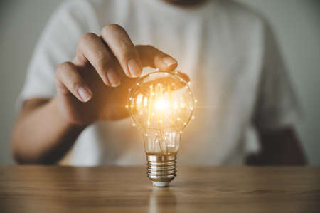 Hand holding light bulb on wood table. Concept of inspiration creative idea thinking and future technology innovationの写真素材