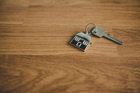 Key and a keychain shaped house on wooden floor in room. Property investment and house mortgage financial real estate conceptの写真素材