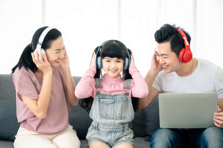 Asian family happy in relax time. Dad and mom with daughter listening music in living roomの写真素材