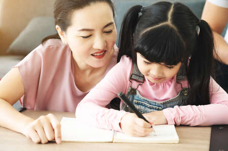 Asian mother helping daughter with homework at living room