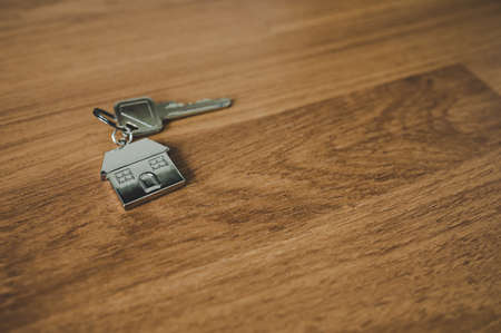 Key and a keychain shaped house on wooden floor in room. Property investment and house mortgage financial real estate conceptの写真素材