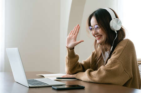Young asian woman in headphone having conversation chatting while using laptop at house. Work at...