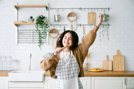 Asian young woman dancing in kitchen room. She happy and relaxing at free time on weekendの写真素材