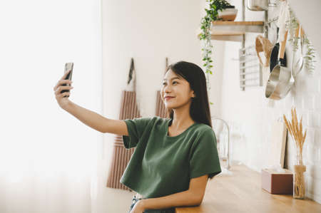 Pretty young asian female with big smile and stand at kitchen room. She having fun taking light...