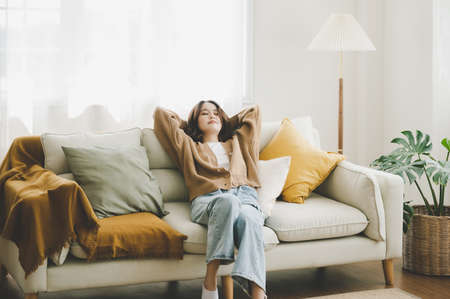 Happy asian woman relaxing on comfortable soft sofa enjoying stress free weekend at home, She stretching on couch thinking of pleasant lazy dayの写真素材