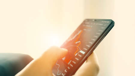 Hand touching screen mobile phone investing stock market application. Financial investment online...