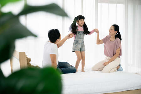 Happy asian family people leisure in bedroom together. Father and mother with daughter relaxing on bed and enjoy funnyの写真素材
