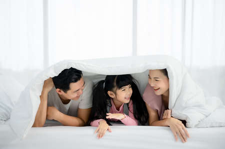 Happy asian family people leisure in bedroom together. Father and mother with daughter relaxing on bed and enjoy funnyの写真素材