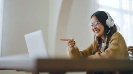 Young asian woman wearing glasses and headset working on computer laptop at house. Work at home,...