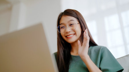 Smiling young asian woman working on laptop at home. Attractive asia female using computer remote studying, watching online education and video callingの写真素材