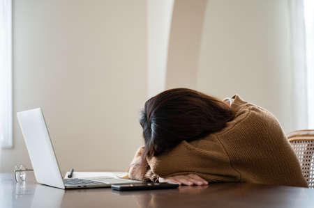 Asian woman lying face down on the table. Overworked tired young asian woman, having eyesight problem after computer laptop workの写真素材