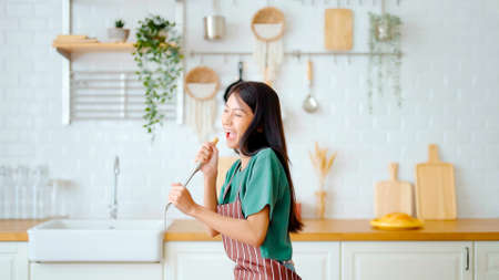 Asian young woman dancing in kitchen room. Female happy and relaxing at free time on weekendの写真素材