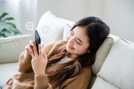 Young asian woman using mobile smartphone in living room. Online live chat chatting on application communication digital media website and social networkの写真素材