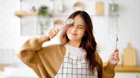 Happy young asian woman wearing apron and standing in kitchen room. Beautiful female smiling and looking at camera feeling confidentの写真素材