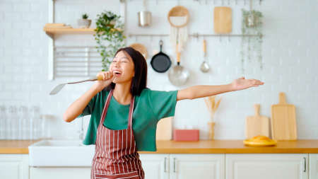 Asian young woman dancing in kitchen room. Female happy and relaxing at free time on weekendの写真素材