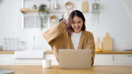 Smiling asian young woman working on laptop at home office. Young asian student using computer remote studying, virtual training, e-learning, watching online education webinar at houseの写真素材
