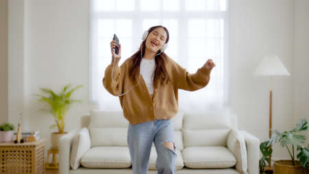 Young asian woman wearing headset and dancing on the floor in living room at home. Happy asia female smile relaxing in house, healthy mental wellness and wellbeingの写真素材