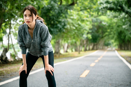 Asian woman wearing jacket and tired engaged in fitness in public park. Her gaze was determined to...