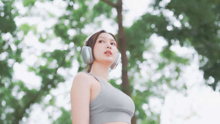 Asian woman trainer is engaged in fitness in public park. Female wearing sport bra and using...
