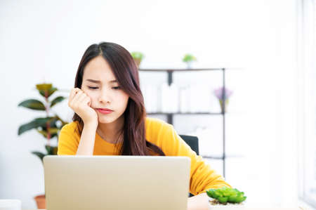 Asian young woman seriously working on computer laptop in house. She thinking find solution problem of workの写真素材
