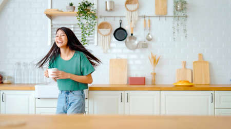Asian young woman dancing in kitchen room. Female happy and relaxing at free time on weekendの写真素材