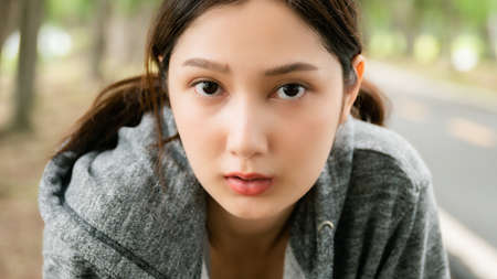 Close up of face asian woman wearing jacket is engaged in fitness in public park. Female tired and look at camera. Healthy lifestyle activity conceptの写真素材