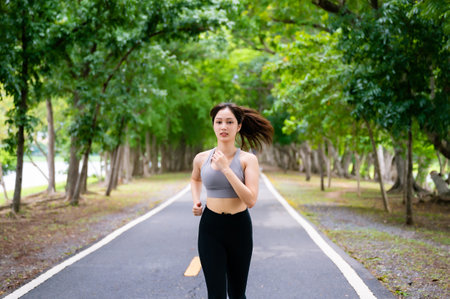 Asian woman running outdoor in public park. Female jogging on the road in morning. Healthy lifestyle concept, sports outdoor activities in parkの写真素材