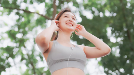 Asian woman trainer is engaged in fitness in public park. Female wearing sport bra and using headphone listening to music. Healthy lifestyle, sports outdoor activities in parkの写真素材