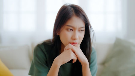 Upset asian woman frustrated by problem with work or relationships, sitting on couch, feeling despair and anxiety, loneliness, having psychological troubleの写真素材
