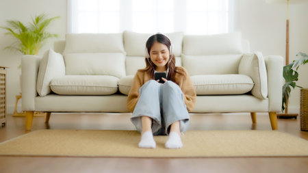 Happy young asian woman relaxing at home. Female smile sitting on sofa and holding mobile smartphone. Girl using video call to friendの写真素材