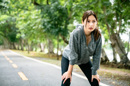 Asian woman wearing jacket and tired engaged in fitness in public park. Her gaze was determined to lose weight. Healthy lifestyle activity conceptの写真素材