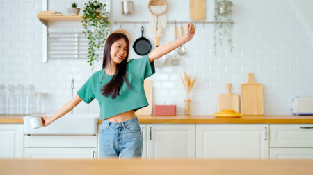 Asian young woman dancing in kitchen room. Female happy and relaxing at free time on weekendの写真素材