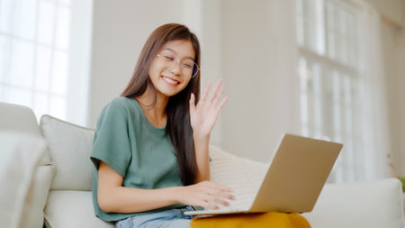 Smiling young asian woman working on laptop at home. Attractive asia female using computer remote studying, watching online education and video callingの写真素材
