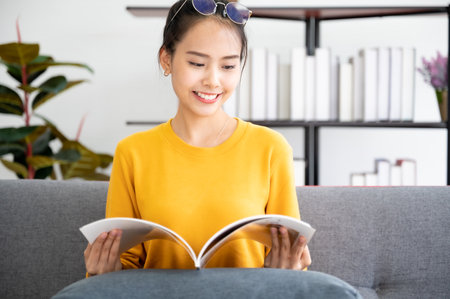 Happy young asian woman reading on the sofa in the living room at homeの写真素材