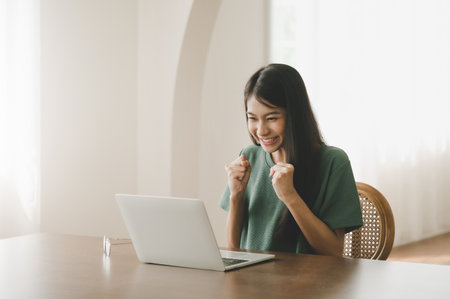 Smiling asian young woman working on laptop at home office. Young asian student using computer remote studying, virtual training, e-learning, watching online education webinar at houseの写真素材