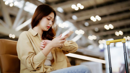 Asian woman waiting for departure at the airport on vacation holiday. Asia female passenger using mobile smart phone and sitting in terminal hall while waiting for her flightの写真素材