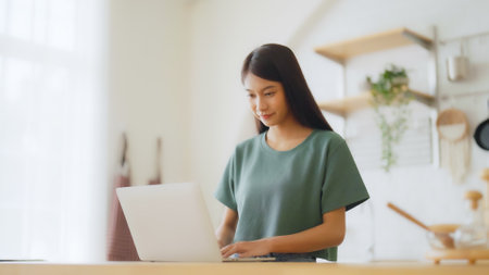 Smiling asian young woman working on laptop at home office. Young asian student using computer remote studying, virtual training, e-learning, watching online education webinar at houseの写真素材