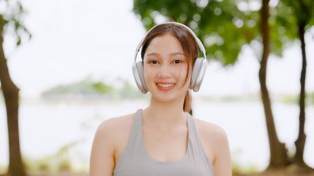 Asian woman trainer is engaged in fitness in public park. Female wearing sport bra and using headphone listening to music. Healthy lifestyle, sports outdoor activities in parkの写真素材