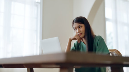 Asian young woman seriously working on computer laptop in house. She thinking find solution problem of workの写真素材