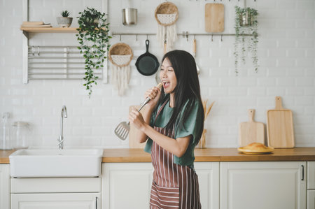 Asian young woman dancing in kitchen room. She happy and relaxing at free time on weekendの写真素材