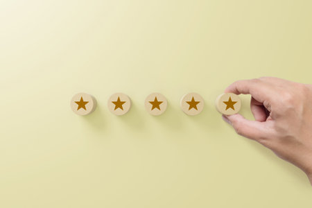 Hand putting wood block with five star symbol to increase rating of company with yellow backgroundの写真素材