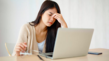 Office syndrome. Overworked tired young asian woman feeling headache, having eyesight problem after computer laptop work. Stressed young woman suffering from fatigue at homeの写真素材