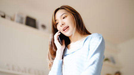 Happy young asian woman speaking on mobile phone at home, Female teen answering call on cellphone while sitting in couch. Asia girl talking on smartphoneの写真素材